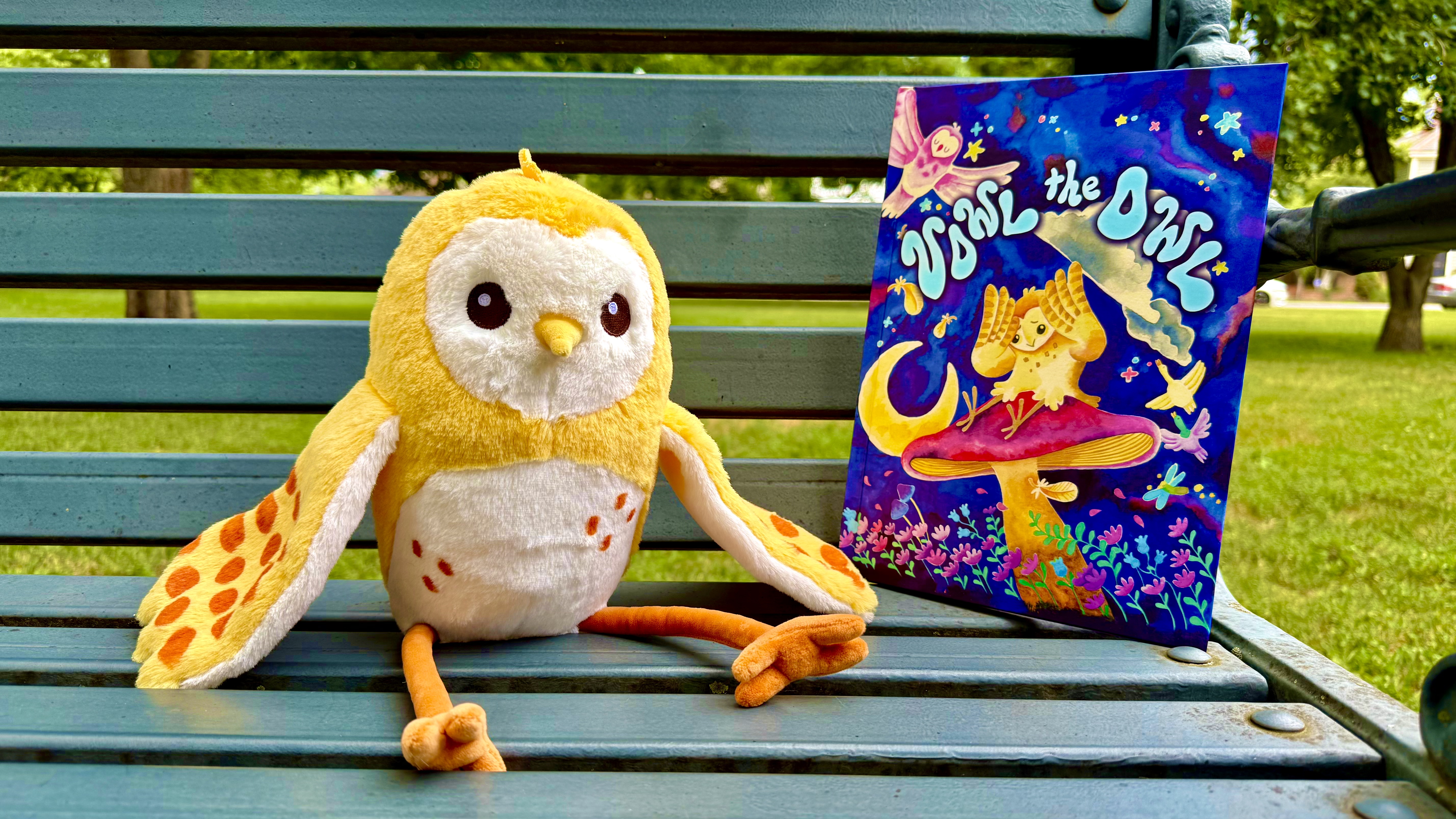 Vowl the Owl plushie sitting beside the book on a park bench